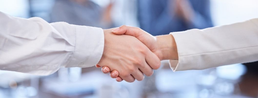 two businesspeople shaking hands with faded background of associates clapping