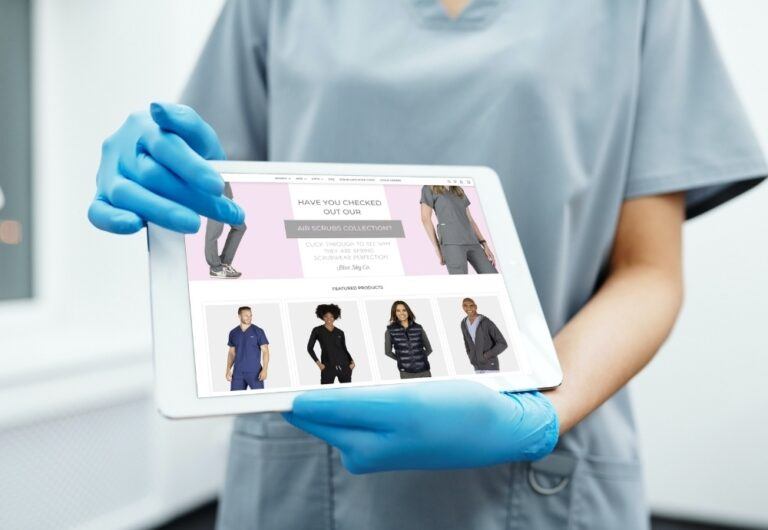 Medical worker in scrubs holding tablet with BlueSkyScrubs.com homepage