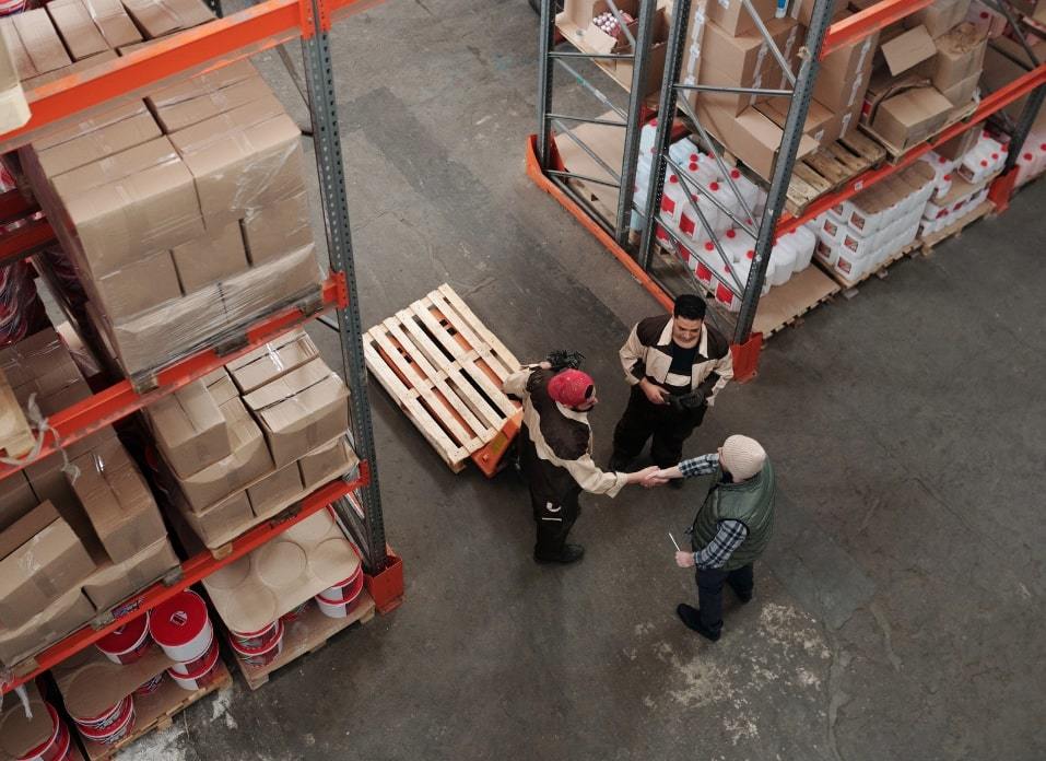 Overtop view of two men in hard hats shaking hands in warehouse