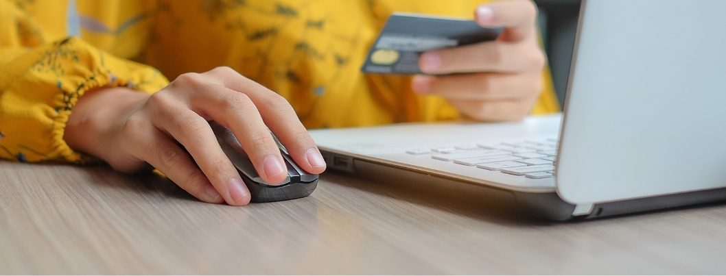 Person using a computer mouse and holding a credit card for online shopping.