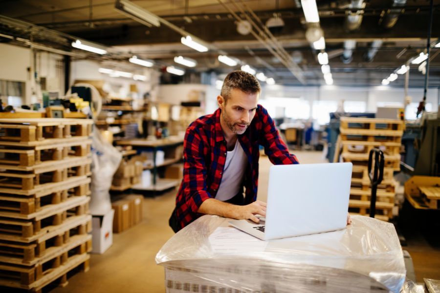 man in warehouse on laptop with pallets in background - BigCommerce redesign