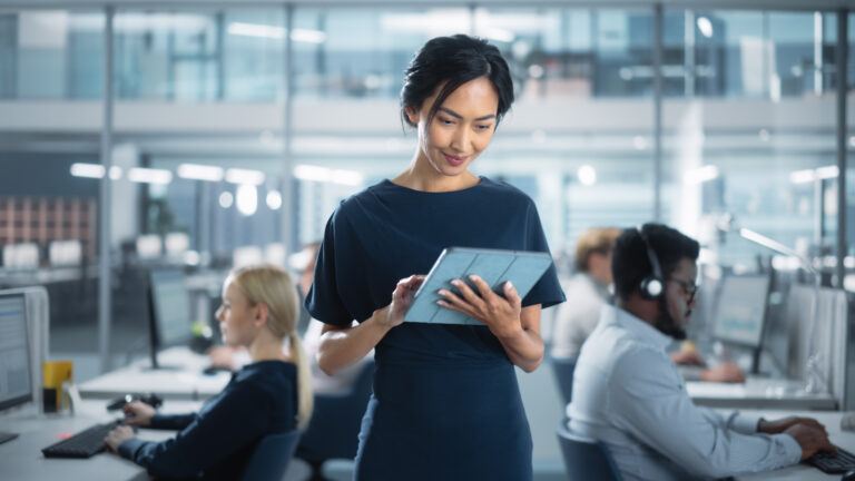 Successful Businesswoman in Stylish Dress Using Tablet Computer, Standing in Modern Diverse Office Working on Financial, Business and Marketing Projects