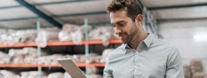 Warehouse manager in front of blurred warehouse background holding tablet and smiling