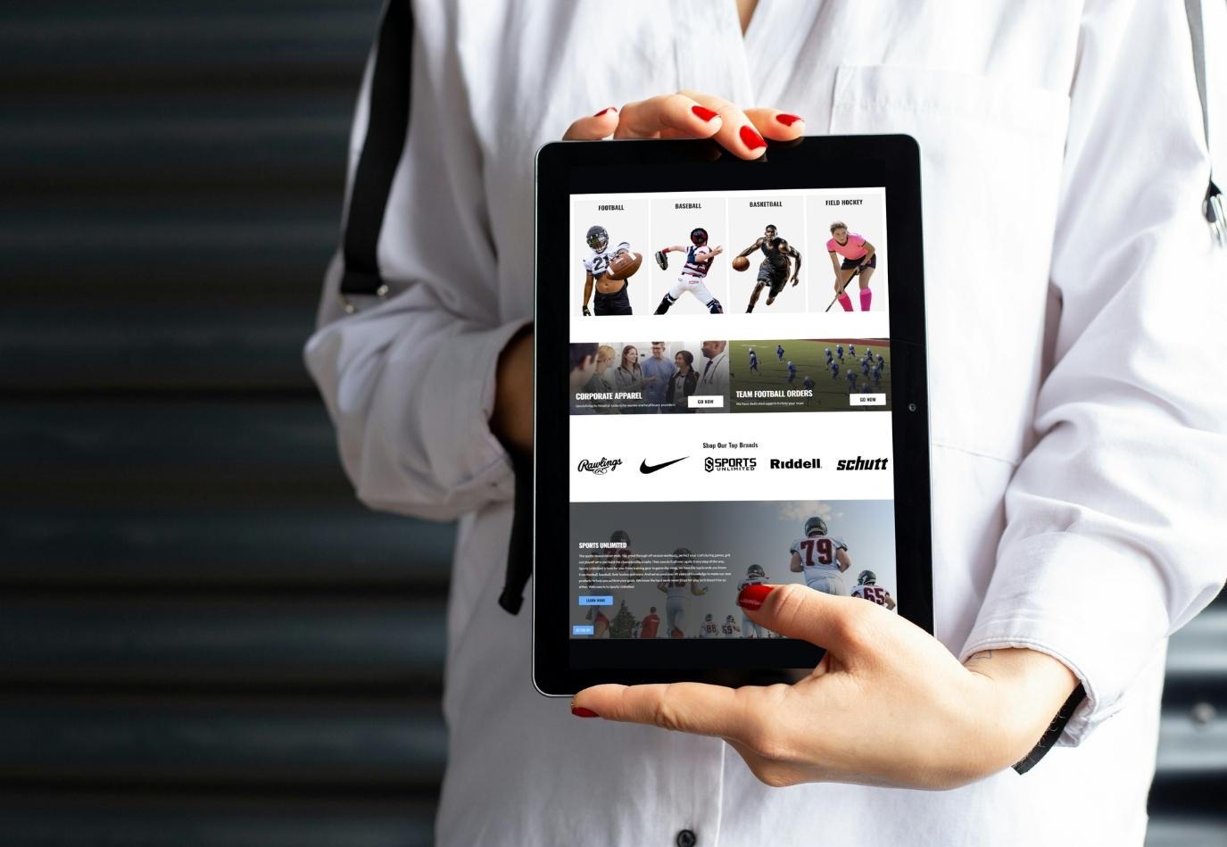 Person in white tracksuit holding tablet with SportsUnlimitedInc.com homepage on screen