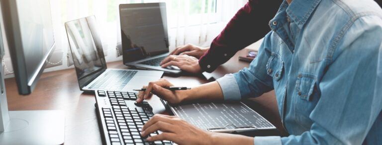 Team of web developers working on desktops and laptops next to each other in office - BigCommerce Design