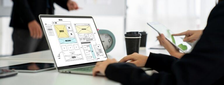 person typing on laptop with website wireframe on screen - surrounded by coworkers - BigCommerce design