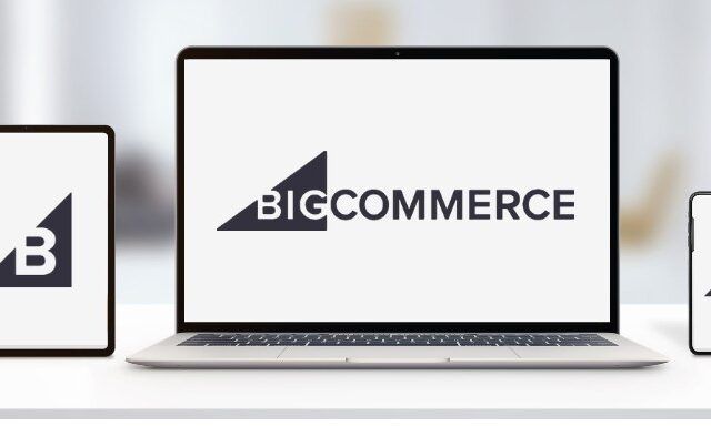 laptop, tablet, and mobile phone on white desk and blurred background showing BigCommerce logo on all screens