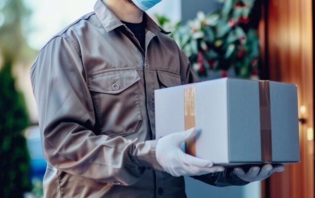 BigCommerce package protection - delivery person wearing gloves holding box at doorstep for delivery