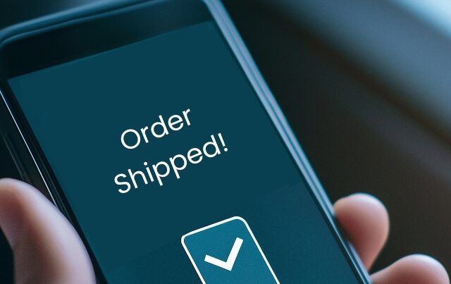 Closeup of hand holding cell phone with "Order Shipped" notification on screen