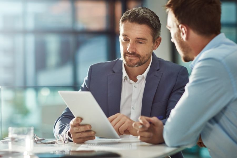 two men meeting at table in corporate setting looking at tablet - Shopify Integrations