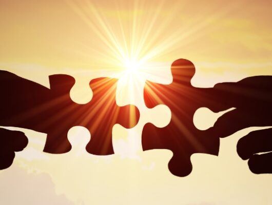 high contrast visual of two hands joining puzzle piece in front of sunset background