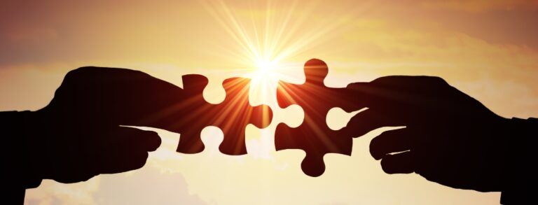 high contrast visual of two hands joining puzzle piece in front of sunset background